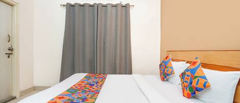 A hotel room with a bed, a headboard, a window with curtains, and an air conditioning unit.