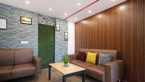Un área de espera moderna con un sofá de cuero marrón, una mesa de madera y una pared verde decorada con obras de arte.