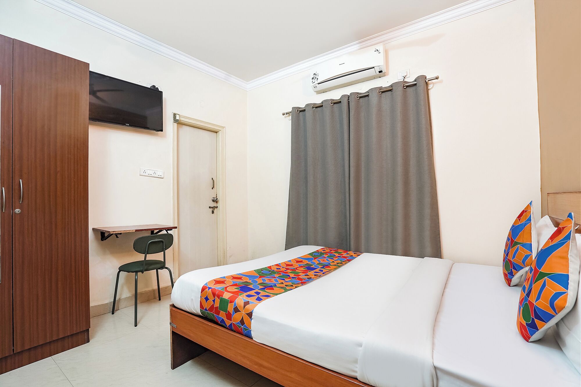 A bedroom with a bed, a desk, a chair, a wardrobe, and an air conditioning unit.