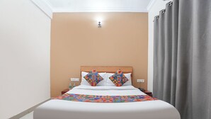Una cama con cabecera de madera, ropa de cama blanca y almohadas con diseños geométricos coloridos.