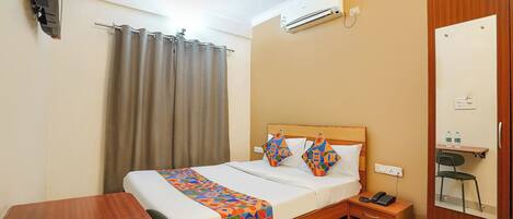 A hotel room with a bed, a desk, a chair, a telephone, a mirror, and a ceiling fan.