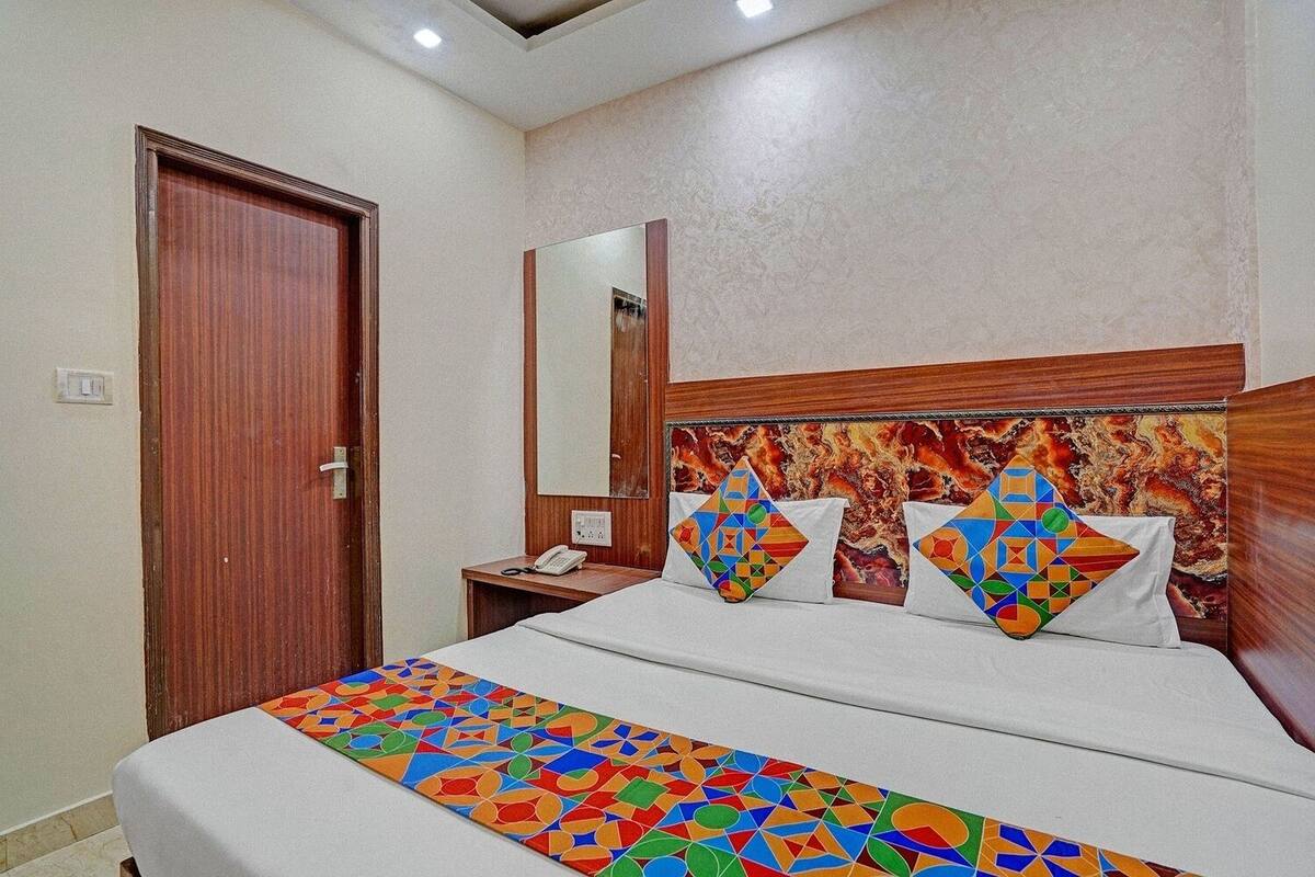 A hotel room with a wooden headboard, a bed with colorful geometric-patterned bedding, a bedside table with a phone, and a mirror on the wall.