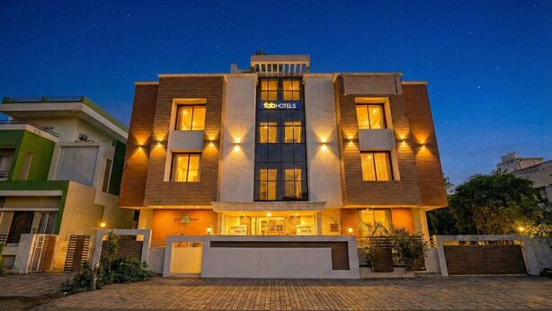 A modern building with a sign for 'fabHOTELS'. It features a central entrance with a covered area, multiple windows on the facade, and is surrounded by a paved area with plants. - Fabhotel Sandalwood Vibes (Bhopal)