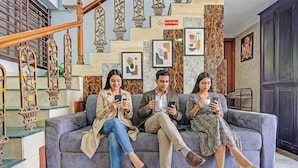 A group of people sitting on a grey sofa in a lobby with a staircase, framed artwork, and a 'No Smoking' sign. - Fabhotel Sandalwood Vibes (Bhopal)