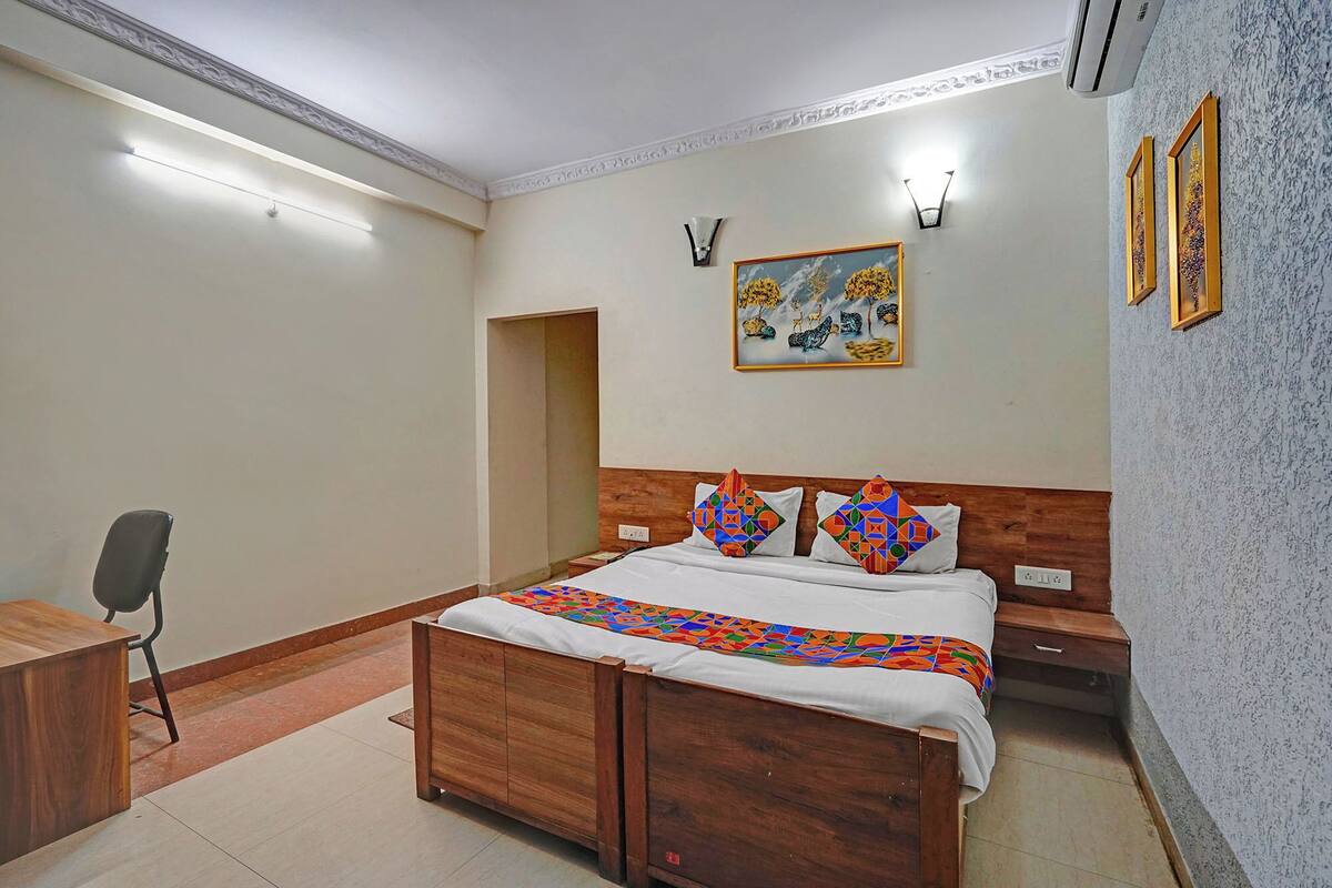 Una camera da letto con un letto di legno, una scrivania e una sedia. Al muro, un quadro e un condizionatore d'aria.