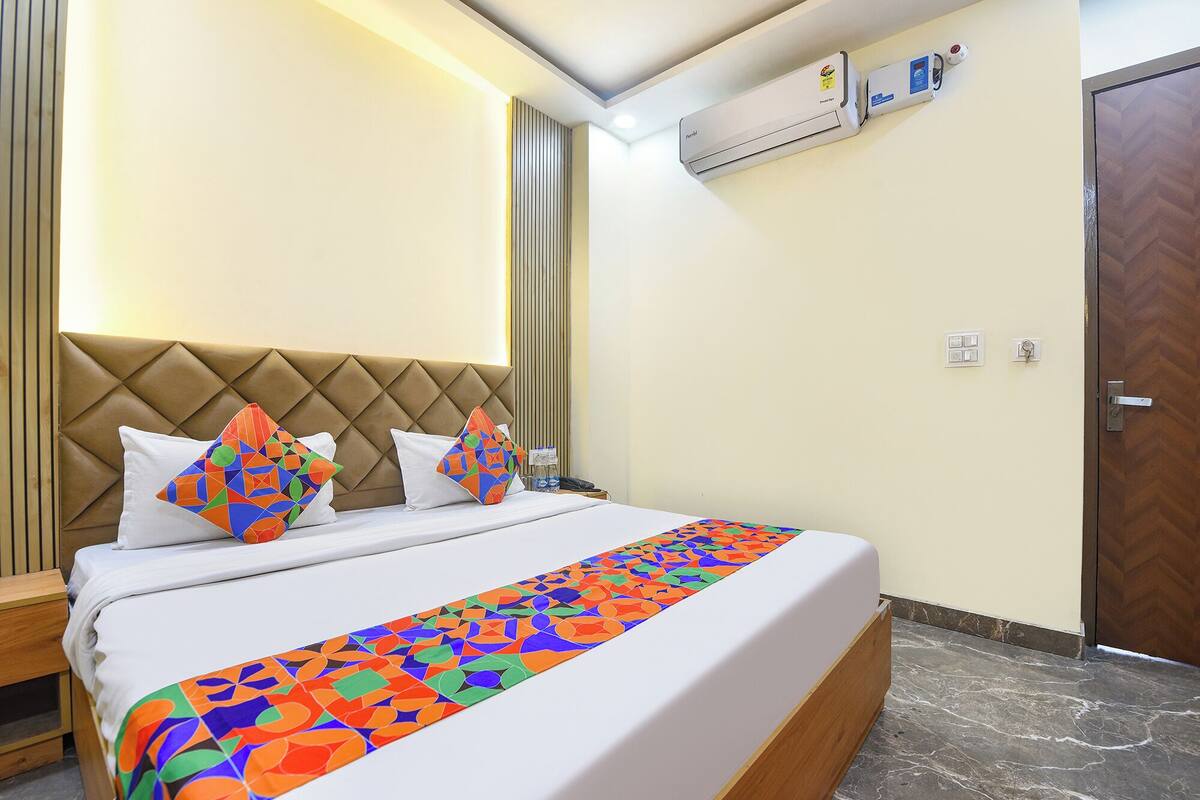 A hotel room with a bed, a headboard, an air conditioning unit, a door, and a marble floor.