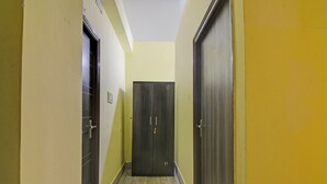 Un couloir étroit, avec une porte en bois au fond, un interrupteur sur le mur et une porte avec une poignée sur le côté gauche.