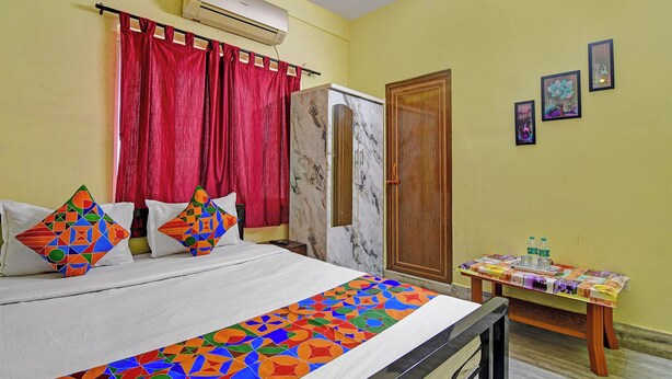 Une chambre d’hôtel avec un lit, un rideau rouge, un climatiseur, une porte en bois et une petite table recouverte d’une nappe.