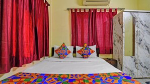 Une chambre d’hôtel avec un lit, des rideaux rouges, une commode en marbre et une couvre-lit aux couleurs vives.