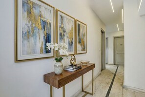 A hallway with three framed abstract paintings, a console table with a vase of white orchids, and a decorative bowl. - Via Red Leaf Stay (New Delhi)