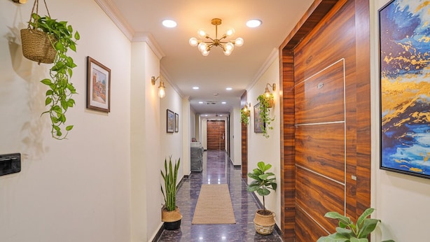 A hallway with a polished marble floor, wooden paneling on one wall, and hanging plants. - FabHotel Havenora - Nr. Maharani Bagh (New Delhi)