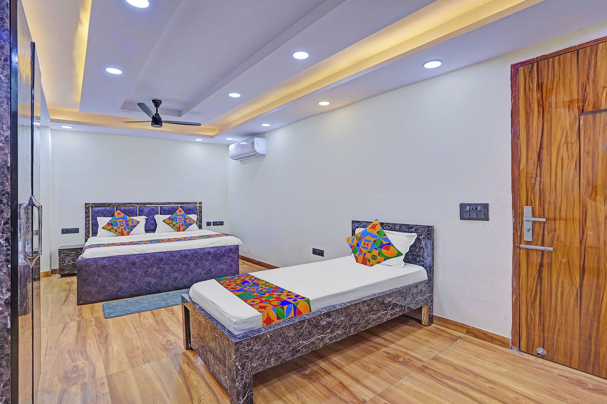 Un dormitorio con dos camas, ventilador de techo, iluminación empotrada, equipo de aire acondicionado y puerta de madera.