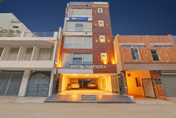 A multi-story hotel with a modern facade, a prominent 'HOTEL HAVENORA' sign, and a covered parking area with two cars. - FabHotel Havenora - Nr. Maharani Bagh (New Delhi)