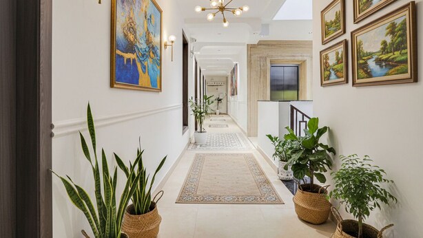 A hallway with a chandelier, framed paintings, and potted plants. - FabHotel Amrit luxury Inn by Amrit Residency (Gurugram)