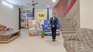 A hotel reception area with a blue sign, a reception desk, a staircase, and a sofa. - Fabhotel Rose Residency (New Delhi)