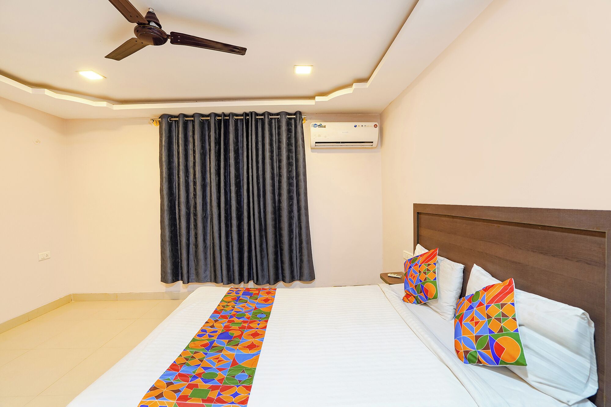 Une chambre d’hôtel avec un lit, un ventilateur de plafond, un appareil de climatisation et un rideau.