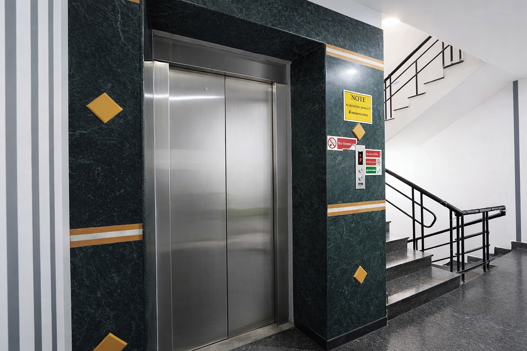 An elevator with a metallic finish, a stairwell with a black railing, and a marble wall with directional signs.
