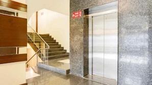 Un ascensor modern amb paret de granit i senyal d'emergència.
