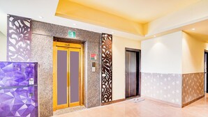 Een hotel lobby met een marmeren vloer, twee liften en een decoratief paneel met een cijfer.'