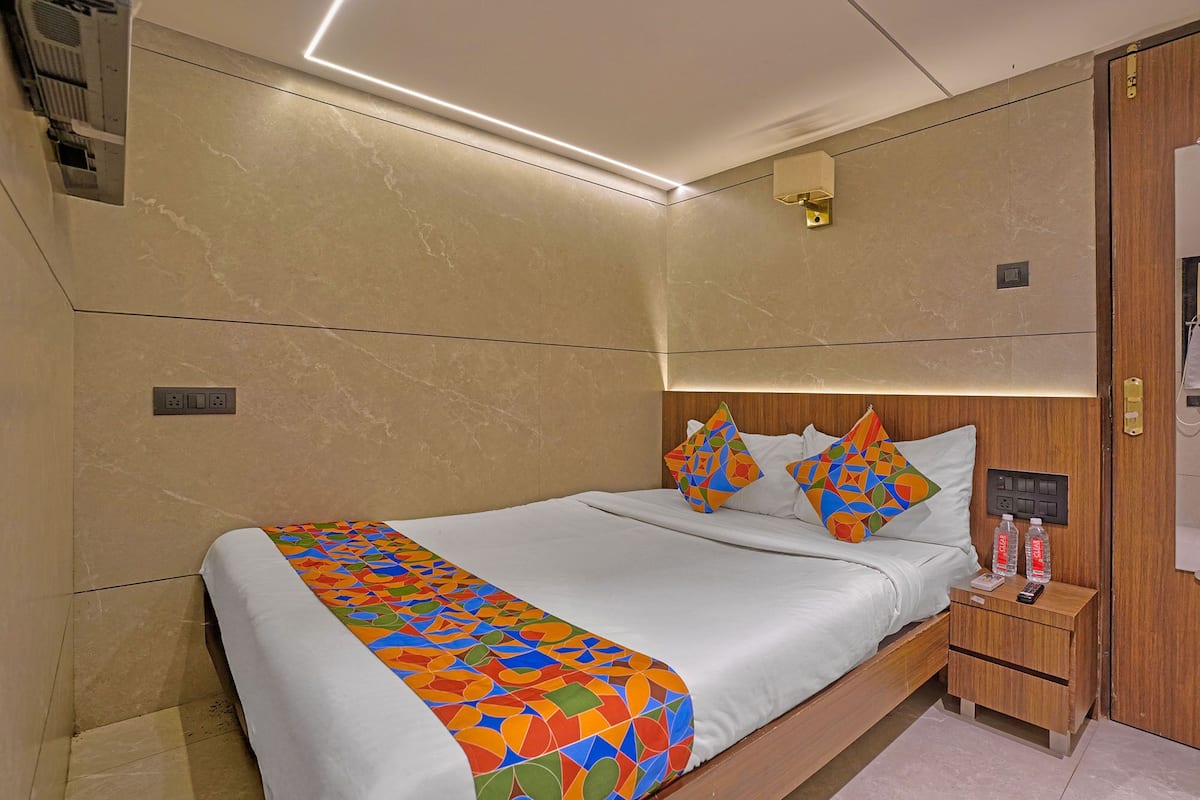 A modern hotel room with a neatly made bed, a bedside table with a remote control, and a wall-mounted light fixture.