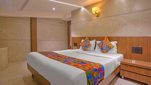 A modern hotel room with a large bed, wooden headboard, and a colorful geometric-patterned bedspread. - Via Woodlands (Mumbai)