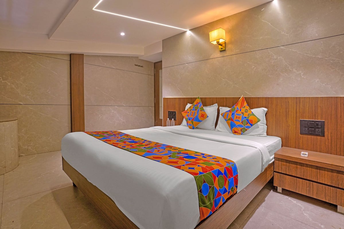 A modern hotel room with a large bed, wooden headboard, and a colorful geometric-patterned bedspread.