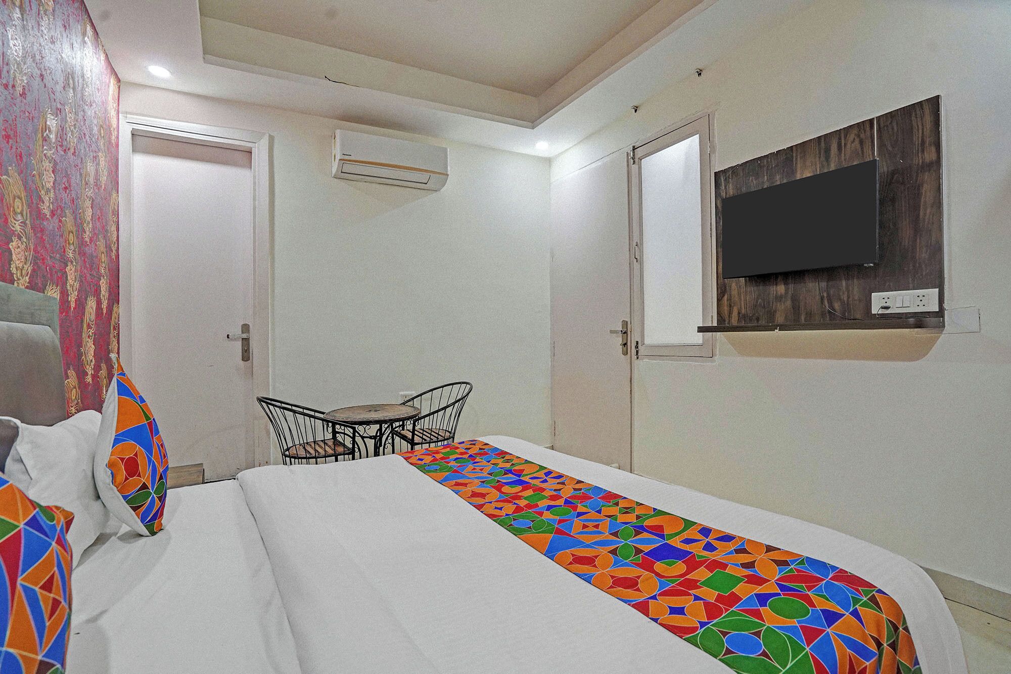 Une chambre d’hôtel comprenant un lit, une petite table avec des chaises, un appareil de climatisation et un téléviseur fixé au mur.