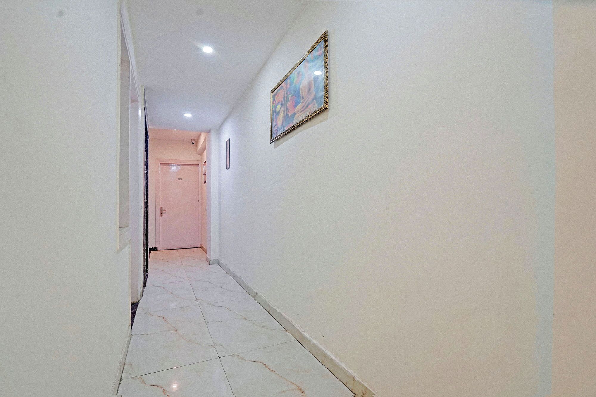 A hallway with a tiled floor, a door at the end, and a framed picture on the wall.