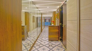 A hotel corridor with a patterned floor, wooden paneling, and a reception desk with a vase of flowers. - Via KR Chennai (Chennai)