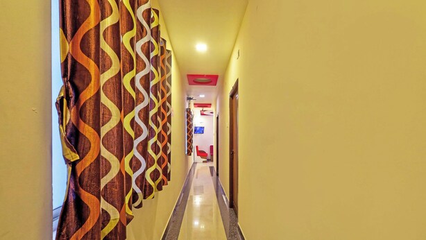 A hotel hallway with patterned curtains, a red seating area, and a television mounted on the wall. - Via KR Chennai (Chennai)
