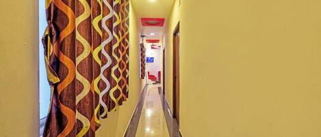 Un corridoio d'albergo con tende a motivi decorativi, una zona salotto rossa e un televisore fissato alla parete.