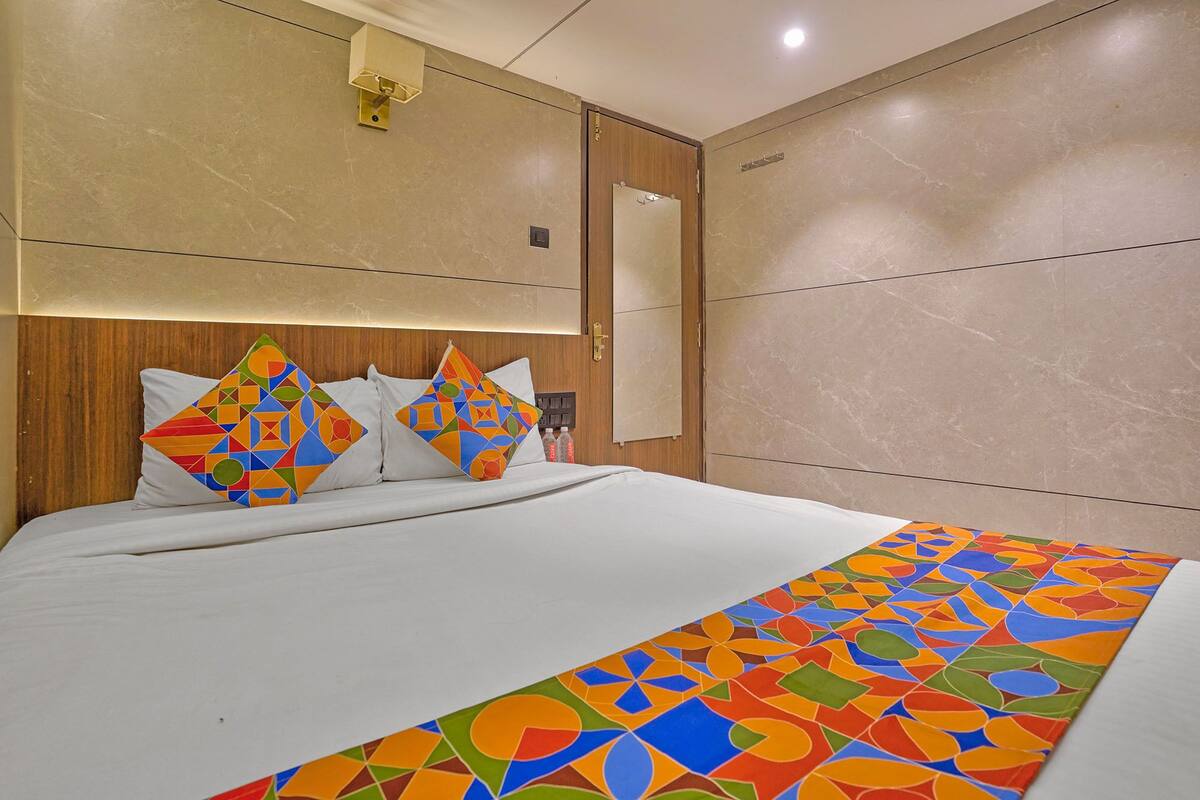 A hotel room with a bed, a headboard, a mirror, and a wall with a geometric-patterned runner.
