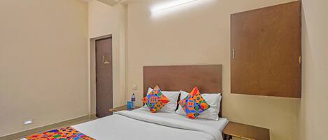 A hotel room with a bed, pillows, a nightstand, a desk, and a door.