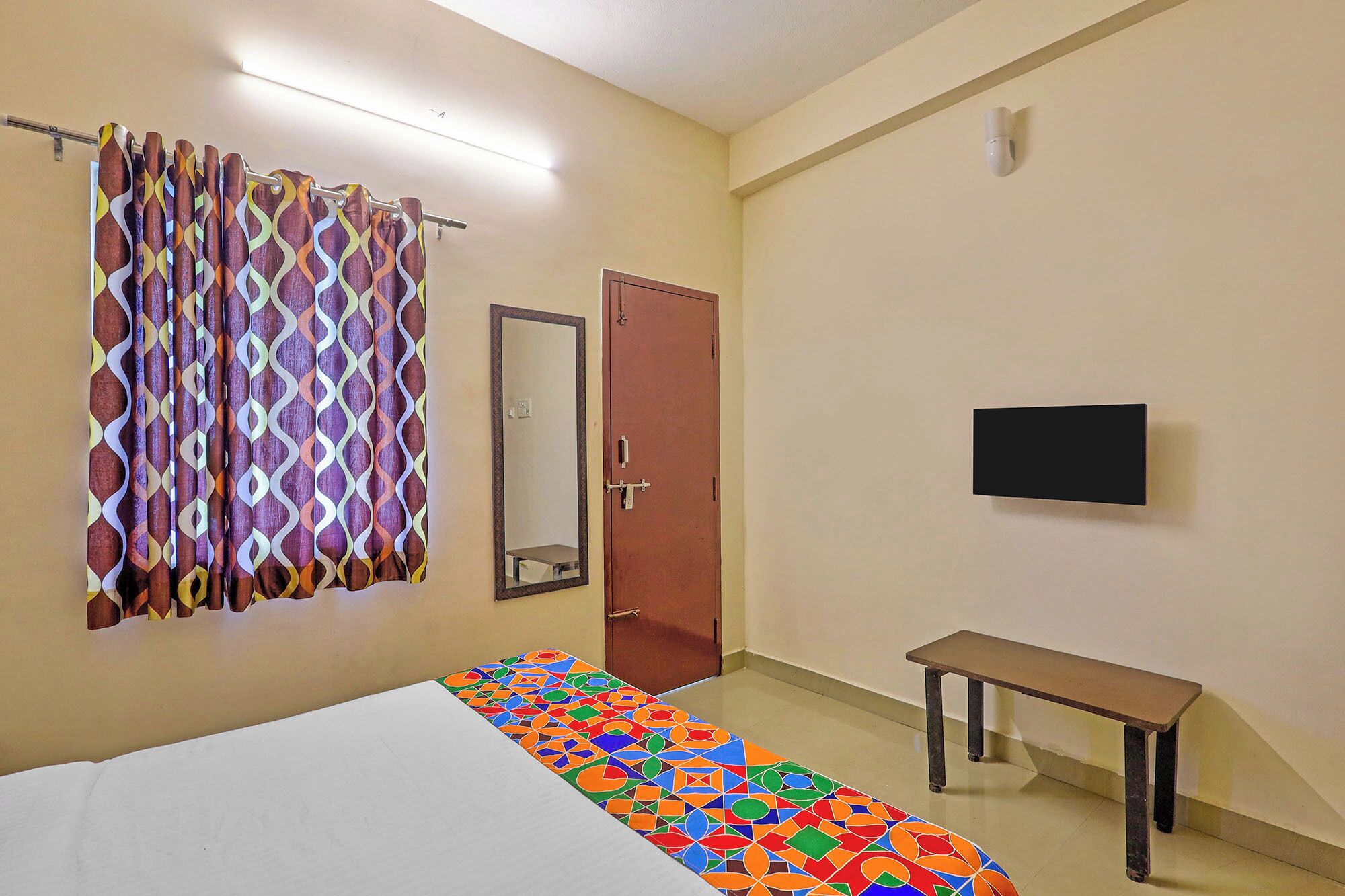 A room with a bed, a mirror, a television, and a bench.