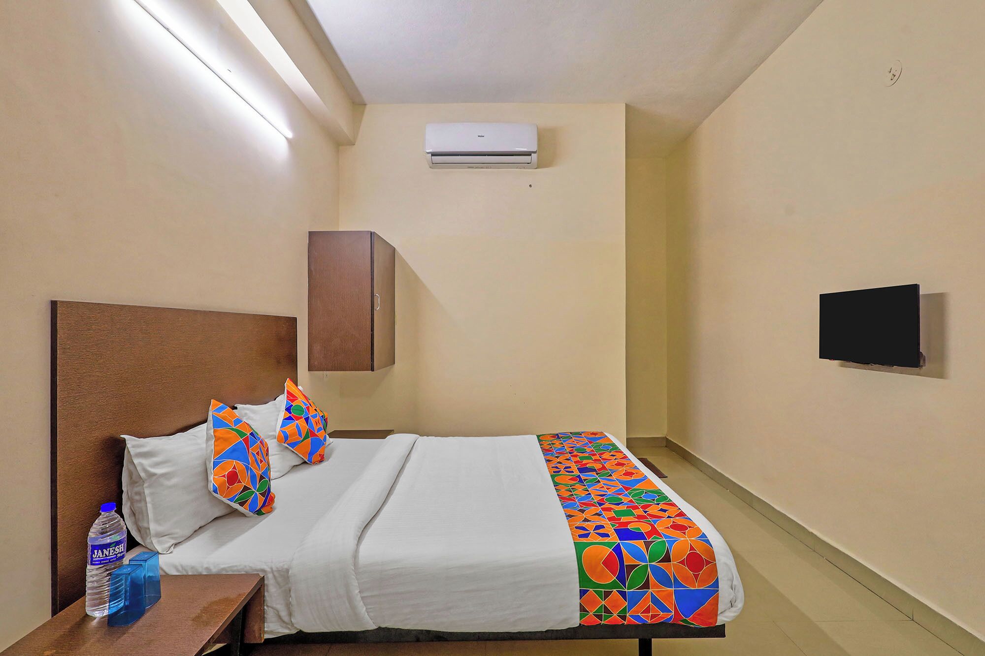 A hotel room with a bed, a water bottle, a TV, and an air conditioner.