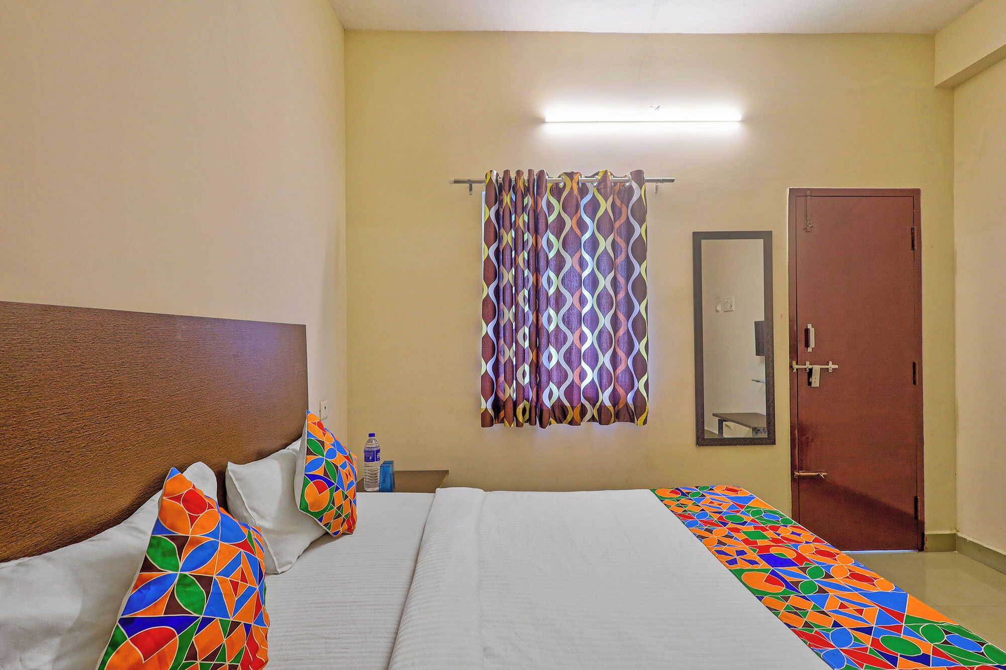 A hotel room with a bed, a mirror, a door, and a curtain.