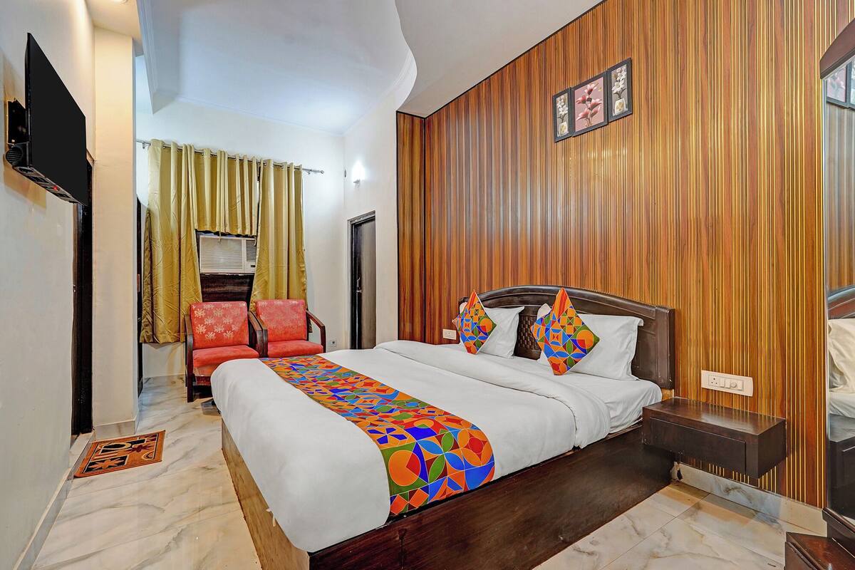 A hotel room with a bed, a wooden panel wall, a TV, and a chair.