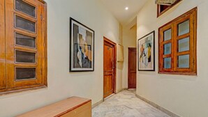 A hallway with wooden doors, a bench, and framed artwork on the walls. - Via Crown DX (New Delhi)