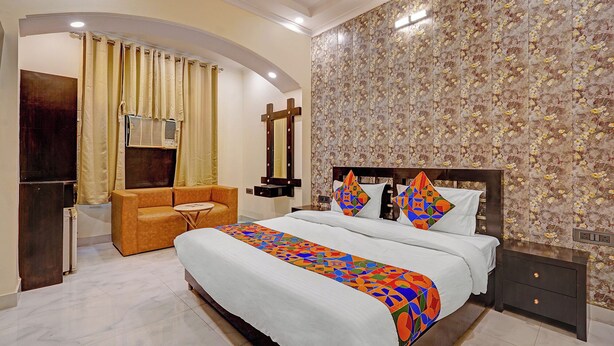 A bedroom with a large bed, a sofa, a small table, and a mirror. - Via Crown DX (New Delhi)