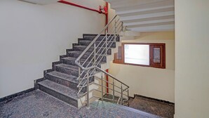 A staircase with metal railings, a red fire hose, and a window with a bulletin board. - Fabhotel Mj International (Lucknow)