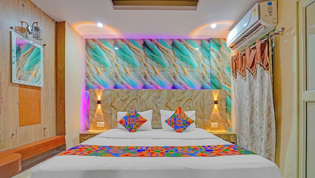 A hotel room with a large bed, marble-patterned headboard, two wall-mounted lamps, and a ceiling light. - Fabhotel Mj International (Lucknow)