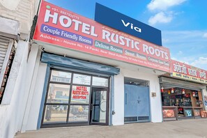 A hotel named 'Rustic Roots' with a reception area, a large signboard advertising various room types, and a visible address.