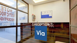 Ein Empfangsbereich mit großem Fenster, einer Rezeption und einer Wandtafel mit Informationen.