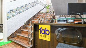 A hotel reception area with a staircase leading to an upper floor, a reception desk, and a view of the outside. - Fabhotel Springwood (Barasat)
