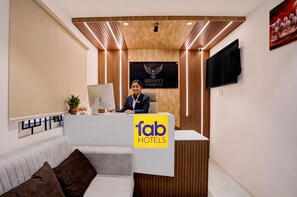 Een receptiebalie in een hotel met een logo, een aan de muur bevestigde televisie en een bank met kussens.