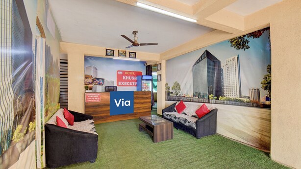 A hotel reception area with a reception desk, a sofa, a coffee table, and a mural of buildings. - Via Royal Stay I (Pune)