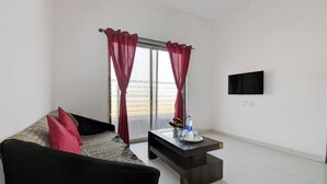 A living room with a sofa, a coffee table, and a TV mounted on the wall. - Via Royal Stay I (Pune)