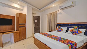 A hotel room with a bed, a TV, a wardrobe, and an air conditioning unit. - Fabhotel Satya (Noida)