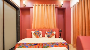 Ein Hotelzimmer mit einem Bett, zwei Kissen, einem Kopfteil, einem Nachttisch, einer Lampe und Vorhängen.