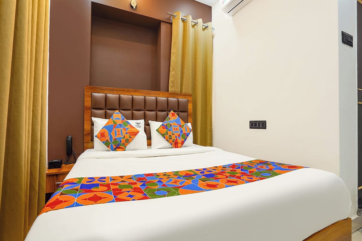 A hotel room with a bed, curtains, a headboard, and a bedside table.